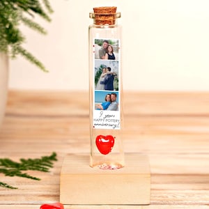 May include: A clear glass bottle with a cork stopper, containing a red heart and photos. The bottle is on a wooden block. The photos are of a couple. Text on the bottle reads "9 years happy pottery anniversary!"