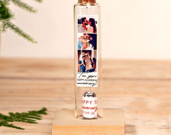 May include: A clear glass test tube with a cork stopper, mounted on a square wooden base. Inside, a vertical strip displays three photographs of a couple and a child, with the text "Ten years HAPPY ALUMINUM anniversary!" and a small rolled paper note.