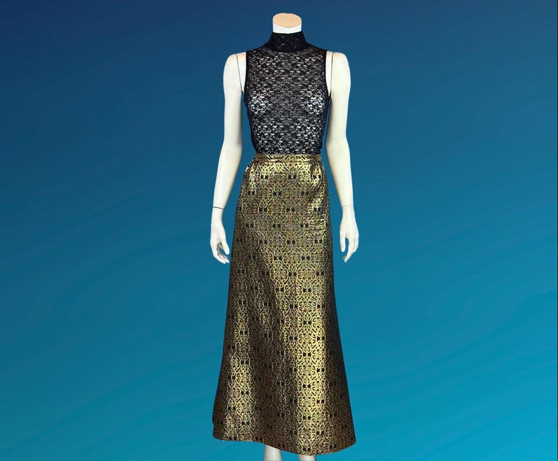 May include: A sleeveless black lace top and a floor-length gold skirt with a repeating black pattern are displayed on a mannequin. The skirt has a slight A-line shape. The mannequin is set against a blue background.