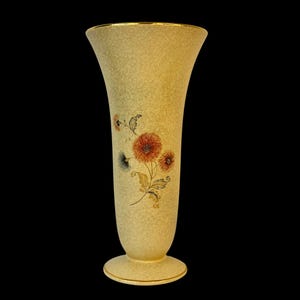 May include: A cream-colored ceramic vase with a gold rim and a floral design featuring orange and yellow flowers. The vase has a flared opening and a rounded base.