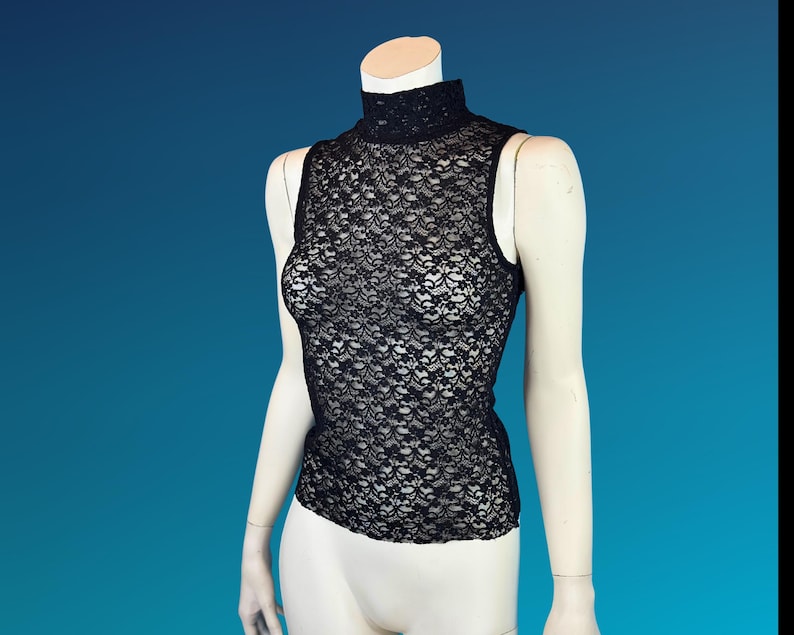 May include: A black sleeveless top made of delicate lace. The top features a high, mock neck and a floral pattern. The garment is displayed on a mannequin against a blue background. The top is a stylish piece of apparel.