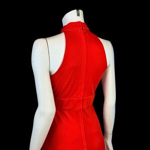 May include: A bright red dress with a high neckline and sleeveless design. The dress has a fitted bodice and a streamlined silhouette, displayed on a mannequin against a black background. The dress is made of a smooth, likely stretchy fabric.