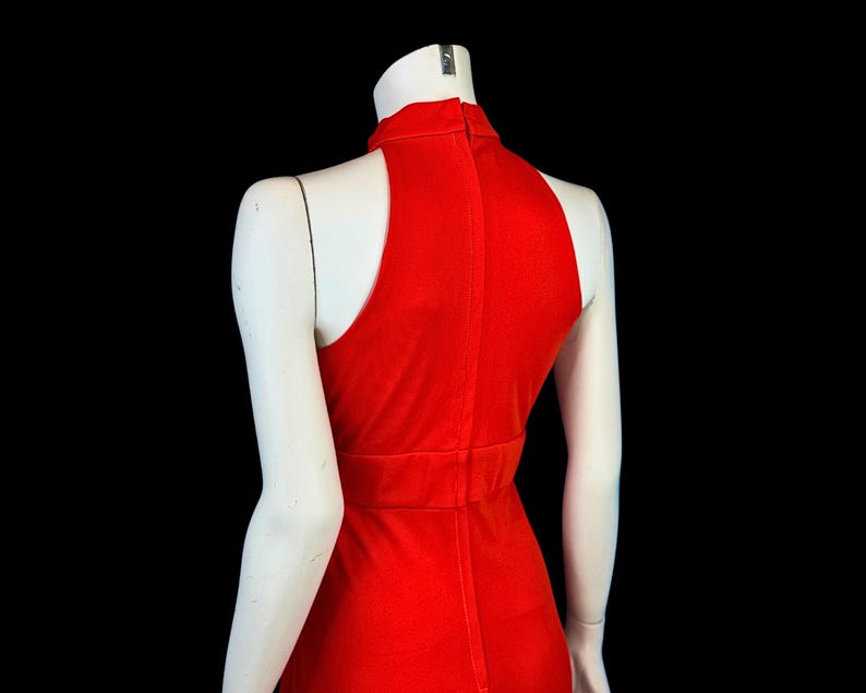 May include: A bright red dress with a high neckline and sleeveless design. The dress has a fitted bodice and a streamlined silhouette, displayed on a mannequin against a black background. The dress is made of a smooth, likely stretchy fabric.