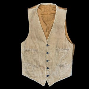 May include: A tan corduroy vest featuring a V-neckline, a five-button front closure, and two welt pockets on the lower front. The garment is lined with a smooth, solid tan fabric that is visible along the inner edges and the collar area.