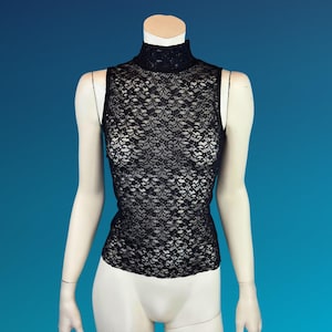 May include: Black sleeveless lace top with a mock neck. The intricate floral lace pattern covers the entire top. The top is displayed on a mannequin against a blue background.
