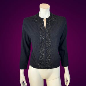 May include: A black cardigan with a beaded design on the front. The cardigan has a V-neck and long sleeves.