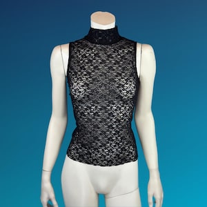 May include: Black sleeveless lace top with a mock neck. The top is displayed on a mannequin against a blue background. The lace pattern is intricate and covers the entire garment.