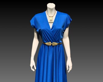 May include: A vibrant blue dress with short sleeves and a V-neckline, featuring a gold-toned geometric pendant necklace and a gold-toned belt with a leaf-shaped buckle centered at the waist, displayed on a mannequin against a dark background.