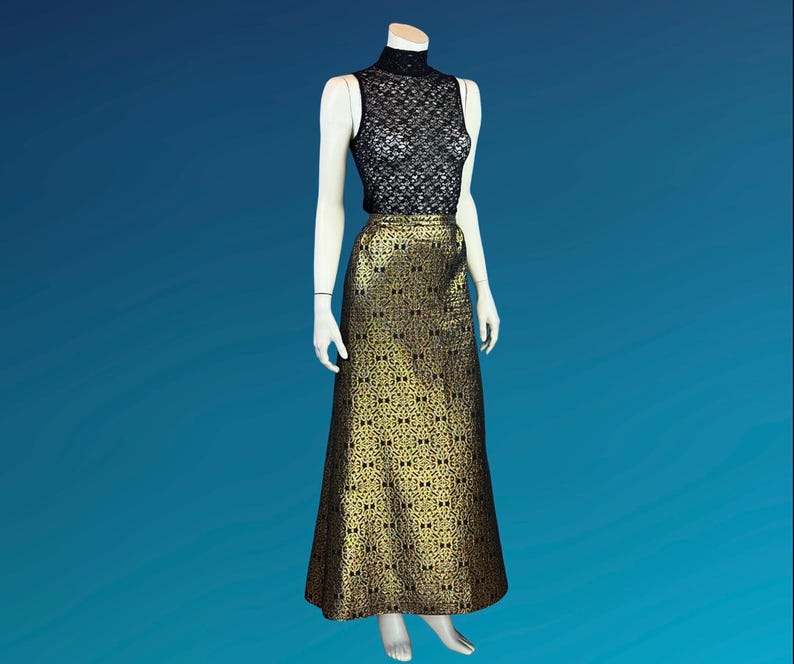 May include: A sleeveless black lace top and a floor-length gold and black patterned skirt are displayed on a mannequin. The skirt has a repeating geometric design. The mannequin is set against a blue background.