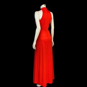 May include: A striking red, full-length dress with a high neck and no sleeves. The gown has a fitted bodice and a flowing skirt, creating an elegant silhouette. The dress is displayed on a mannequin against a black background.
