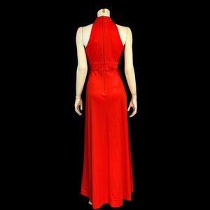 May include: A striking red halter-neck maxi dress. The dress has a high neckline, a fitted bodice, and a flowing skirt. The dress is displayed on a mannequin against a black background, highlighting its elegant design and silhouette.