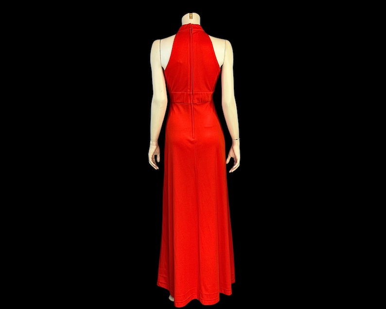 May include: A striking red halter-neck maxi dress. The dress has a high neckline, a fitted bodice, and a flowing skirt. The dress is displayed on a mannequin against a black background, highlighting its elegant design and silhouette.