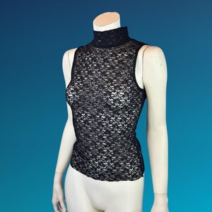 May include: Black sleeveless lace top with a high neckline. The top is displayed on a mannequin against a blue background. The lace pattern is intricate and detailed, creating a delicate and elegant look.