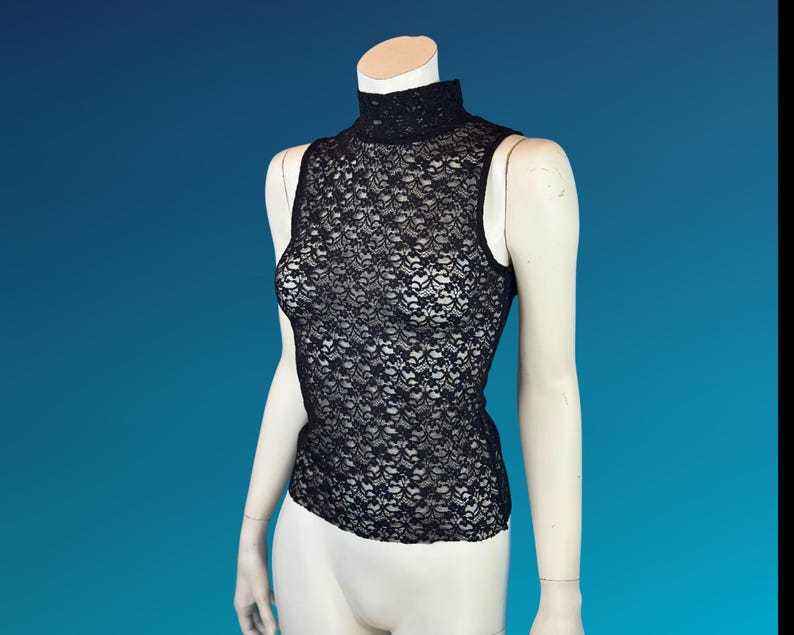 May include: Black sleeveless lace top with a high neckline. The top is displayed on a mannequin against a blue background. The lace pattern is intricate and detailed, creating a delicate and elegant look.