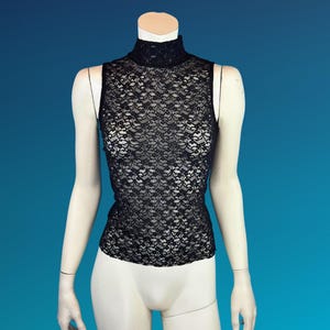 May include: A black lace sleeveless top with a mock neck. The top is displayed on a mannequin against a blue background. The lace pattern is intricate and detailed, creating a delicate and elegant look.