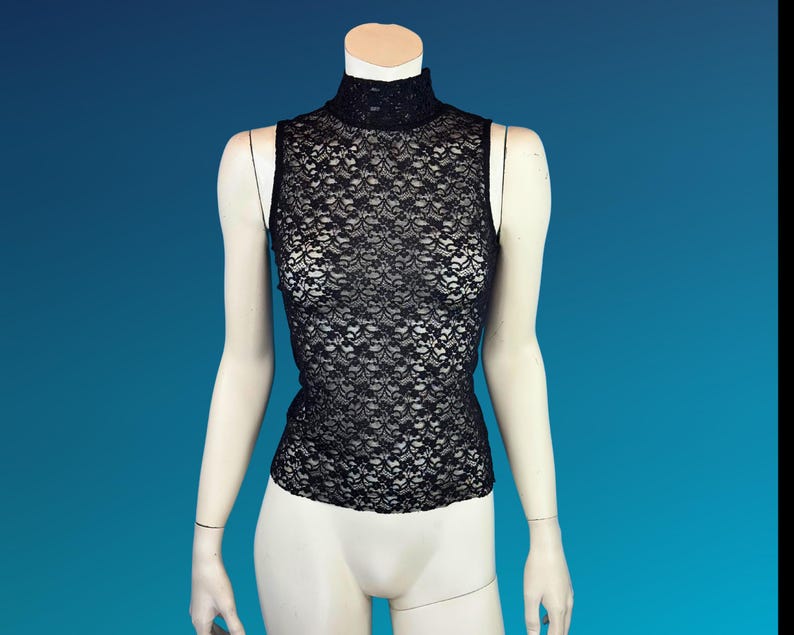 May include: A black lace sleeveless top with a mock neck. The top is displayed on a mannequin against a blue background. The lace pattern is intricate and detailed, creating a delicate and elegant look.