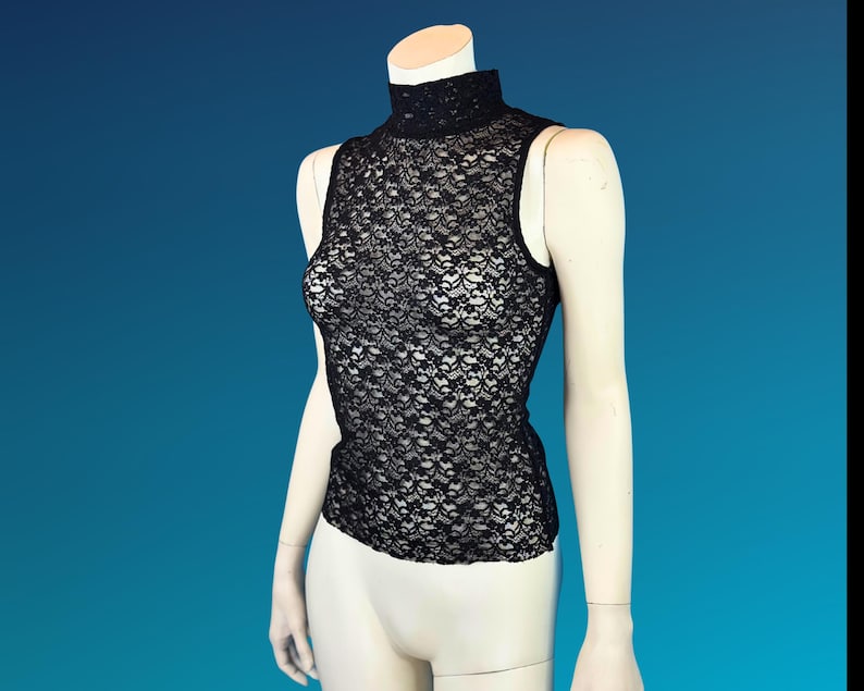 May include: Black sleeveless lace top with a high neckline. The intricate floral lace pattern covers the entire top. The top is displayed on a mannequin against a blue background.