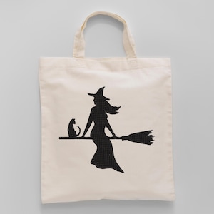 May include: Off-white canvas tote bag featuring a black silhouette of a witch riding a broom with a black cat. The witch is wearing a pointed hat and dress. The tote bag has two handles.
