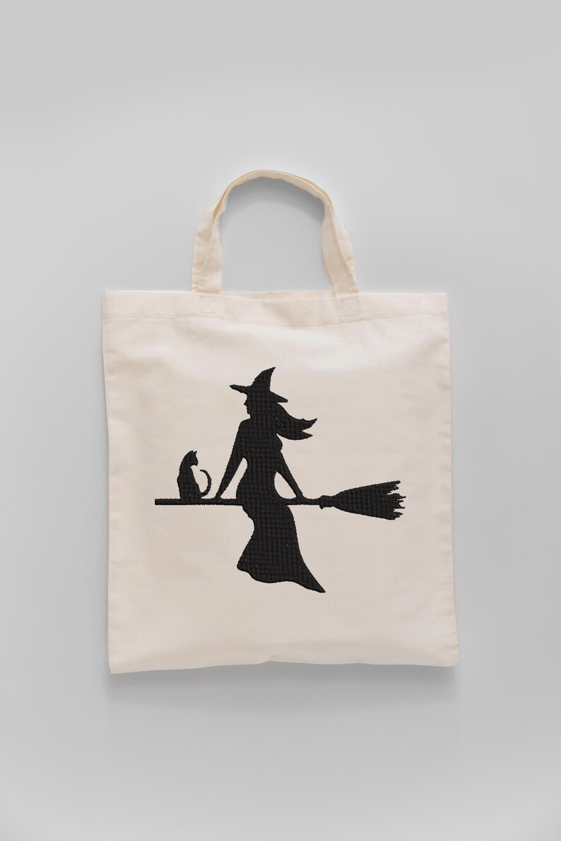 May include: Off-white canvas tote bag featuring a black silhouette of a witch riding a broom with a black cat. The witch is wearing a pointed hat and dress. The tote bag has two handles.