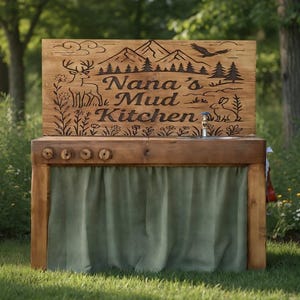 Puede incluir: Una cocina de juegos de exterior de madera con un letrero que dice "Nana's Mud Kitchen". El letrero presenta imágenes de montañas y bosques. La cocina tiene un fregadero y una cortina verde. La estructura está ubicada en un área cubierta de hierba.