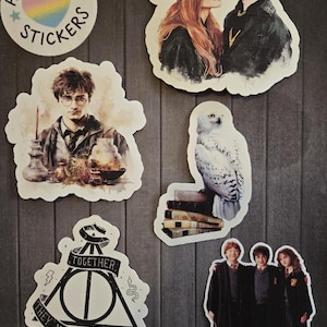 May include: A collection of stickers featuring characters and symbols from a fantasy series. Includes a sticker with the text "Heart Star Stickers" and a rainbow heart, along with images of a snowy owl, and a group of three people.
