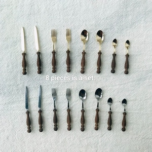 May include: A set of eight pieces of silverware, including knives, forks, and spoons, arranged on a white surface. The silverware features dark brown wooden handles and silver-colored metal blades and bowls. The text "8 pieces is a set" is visible.