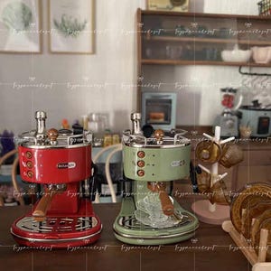 Könnte beinhalten: Zwei Espressomaschinen, eine rote und eine grüne, stehen nebeneinander auf einer Holzoberfläche. Die rote Maschine hat einen silbernen Deckel und einen Holzgriff. Die grüne Maschine hat einen silbernen Deckel und einen Holzgriff. Beide haben ein Delonghi-Logo.