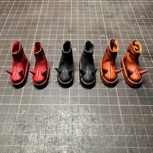 Może przedstawiać: Sześć miniaturowych butów w rzędzie, każdy w unikalnym kolorze. Buty są czerwone, czarne i pomarańczowe i mają kolczasty kolec z boku. Buty są prawdopodobnie przeznaczone dla lalki lub innej małej figurki.