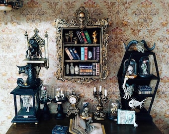 May include: A gothic-themed display featuring a gold-framed bookshelf with miniature books and skulls. Other items include a black coffin-shaped shelf, glass domes, a clock, and a candelabra, all arranged on a wooden surface against a floral wallpaper.