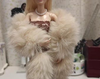 May include: A doll with blonde hair, wearing a pearl headband, earrings, and necklace. The doll is dressed in a brown patterned dress and a cream-colored faux fur stole.