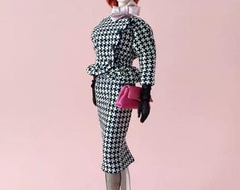 May include: A fashion doll in a black and white houndstooth suit, black beret, and pink bow tie. The doll holds a pink purse and wears black gloves and fishnet stockings. The doll has red hair and is on a black stand.