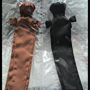 May include: Two long, narrow, satin-like fabric sleeves or covers, one in a rich brown and the other in black. Each piece features a rounded top section, small side tabs, and a straight, elongated body, all individually sealed in clear plastic bags.