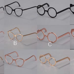 May include: A selection of eyeglasses in diverse styles and colours. The top row presents black frames, including round, cat-eye, and heart-shaped designs. The bottom rows display gold and rose-gold frames in similar shapes, offering a range of eyewear options.