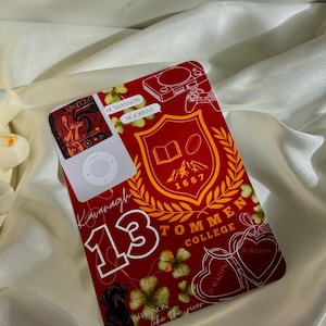 May include: A red iPod with a custom design. The design includes the text "Kavanagh 13" and "Tommen College", a crest, shamrocks, and a black dog illustration. The iPod is on a white satin surface.