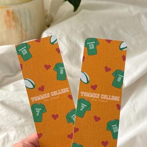 May include: Two orange bookmarks with a pattern of green jerseys, red hearts, and rugby balls. The text "TOMMEN COLLEGE" and player names and numbers are visible on the bookmarks.