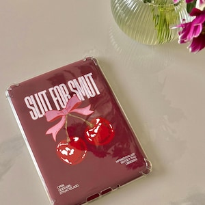 Puede incluir: Una funda de tableta burdeos con borde transparente. La funda presenta el texto "SLUT FOR SMUT" en blanco, junto con un lazo rosa y dos cerezas rojas. El texto adicional incluye "OPEN GOODGRL STFUATDLAGG" y "MASKEDSTALKER SIXFOOTTWO OBSESSIVE."