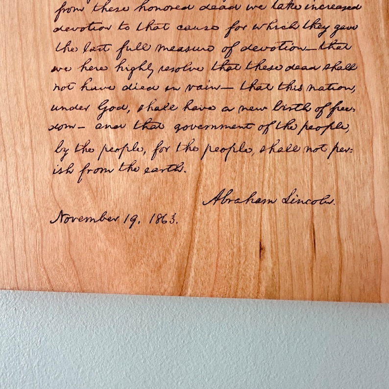 May include: A close-up of a wooden plaque with a handwritten quote from Abraham Lincoln. The quote reads, "from these honored dead we take increased devotion to that cause for which they gave the last full measure of devotion - that these dead shall not have died in vain - that this nation, under God, shall have a new birth of freedom - and that government of the people, by the people, for the people, shall not perish from the earth." The quote is dated November 19, 1863.