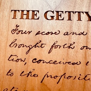 May include: A close-up of a wooden plaque with the text "THE GETTY" engraved in large letters. Below the text is a handwritten quote that reads "Four score and brought forth on tion, conceived i to the proposite".