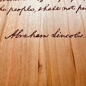 May include: A close-up of a wood surface with the text "...of the people, shall not perish..." and the signature "Abraham Lincoln."