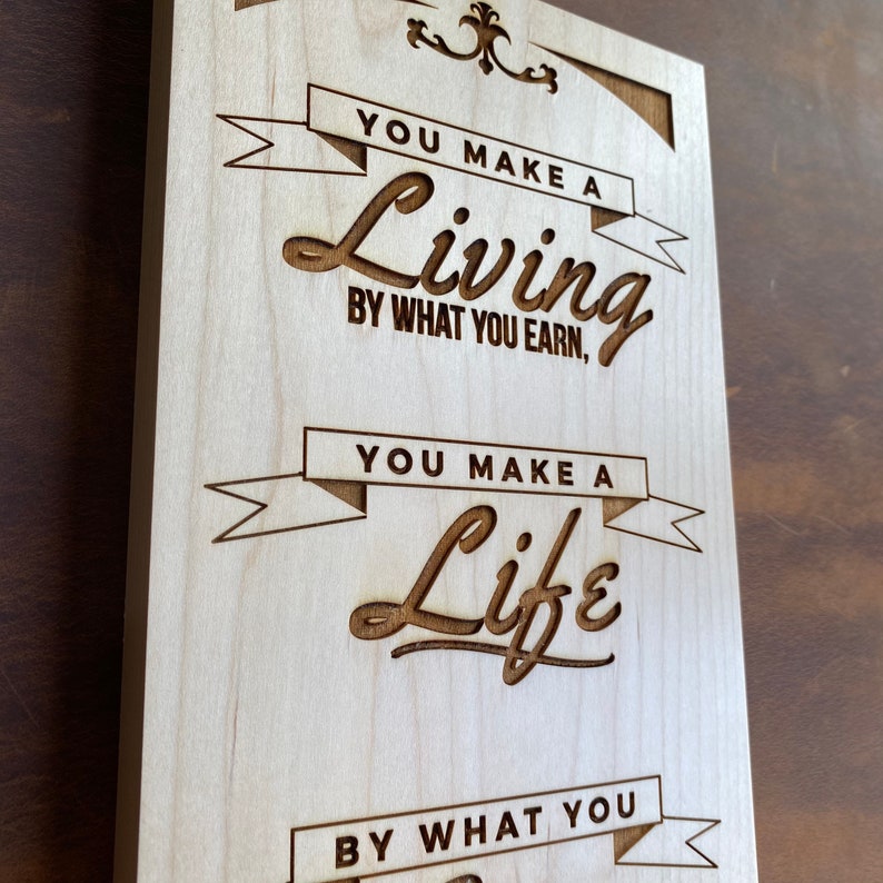 Op de afbeelding: Een houten bord met de tekst "You make a living by what you earn, you make a life by what you give." De tekst is in een vintage lettertype en is met een laser in het hout gegraveerd.
