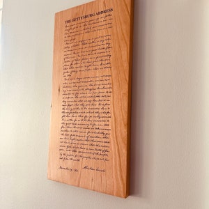 May include: A wooden plaque with the Gettysburg Address engraved in black ink. The text reads: "Four score and seven years ago our fathers brought forth on this continent, a new nation, conceived in Liberty, and dedicated to the proposition that all men are created equal..."