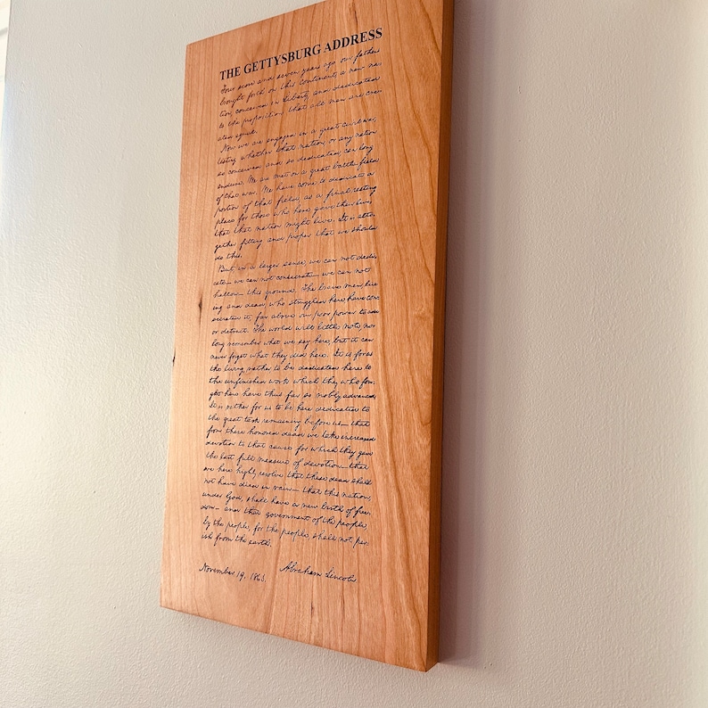 May include: A wooden plaque with the Gettysburg Address engraved in black ink. The text reads: "Four score and seven years ago our fathers brought forth on this continent, a new nation, conceived in Liberty, and dedicated to the proposition that all men are created equal..."