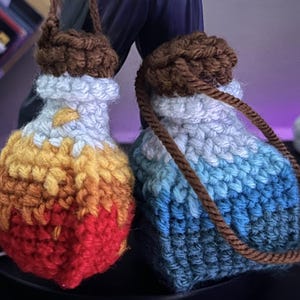 May include: Two handmade crochet pouches. One is red, orange, and yellow, the other is blue and white. Both have brown tops and matching cords. The pouches are likely for small items or decorative purposes.