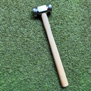May include: A metal ball-peen hammer with a polished steel head and a light-colored wooden handle. The hammer is designed for shaping metal and other materials. The handle is approximately 10 inches long.