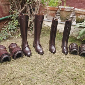 Puede incluir: Un conjunto de botas de montar de cuero marrón oscuro y protectores de pierna a juego. Las botas altas presentan una caña estructurada con cierre de cremallera frontal, mientras que los cuatro protectores tienen formas curvas.