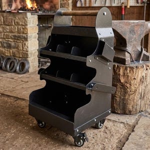May include: Black metal tool cart with a wooden handle and multiple storage compartments. The cart has wheels for easy movement and is designed for workshop use. The cart is in a blacksmith's workshop, with a forge and anvil in the background.