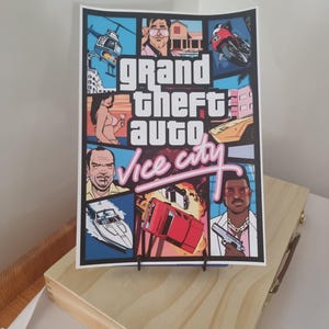 May include: A rectangular poster featuring the Grand Theft Auto Vice City logo in the centre, surrounded by a collage of comic-style illustrations including a helicopter, a motorcycle, a speedboat, a red car, and various character portraits.