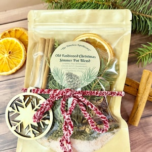 May include: A clear cellophane bag containing an "Old Fashioned Christmas Simmer Pot Blend" with cinnamon sticks, dried orange slices, and a wooden snowflake ornament tied with a red and white pipe cleaner bow. The label reads "The Timeless Apothecary."