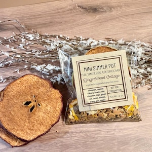 May include: A clear plastic pouch labeled Mini Simmer Pot Gingerbread Cottage containing dried ingredients like cinnamon, roasted chicory, licorice root, ginger, cloves, allspice, orange peel, and apples, with a net weight of .5 oz.