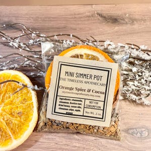 May include: A clear plastic pouch containing a mini simmer pot mix labeled Orange Spice & Cocoa by The Timeless Apothecary. The ingredients include chamomile, cinnamon, licorice root, dried honey, cacao nibs, cinnamon chips, apple, and orange. Net Wt. .5 oz.